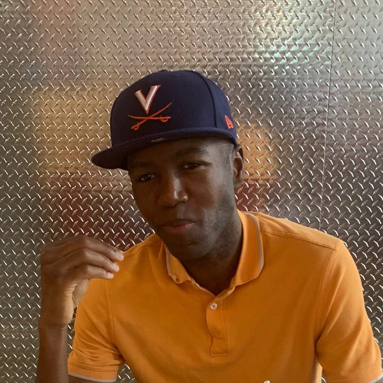 Head-and-shoulders portrait of Pierre wearing an orange polo and a baseball cap.